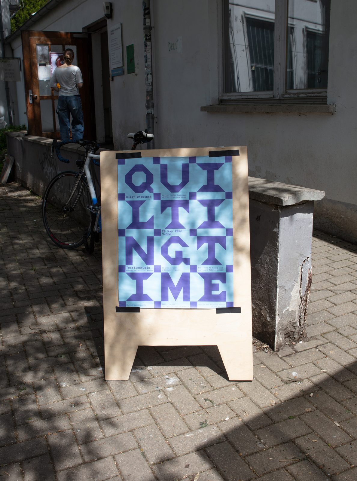 The workshop poster taped to a wooden sign outside the Textilwerkstatt building.