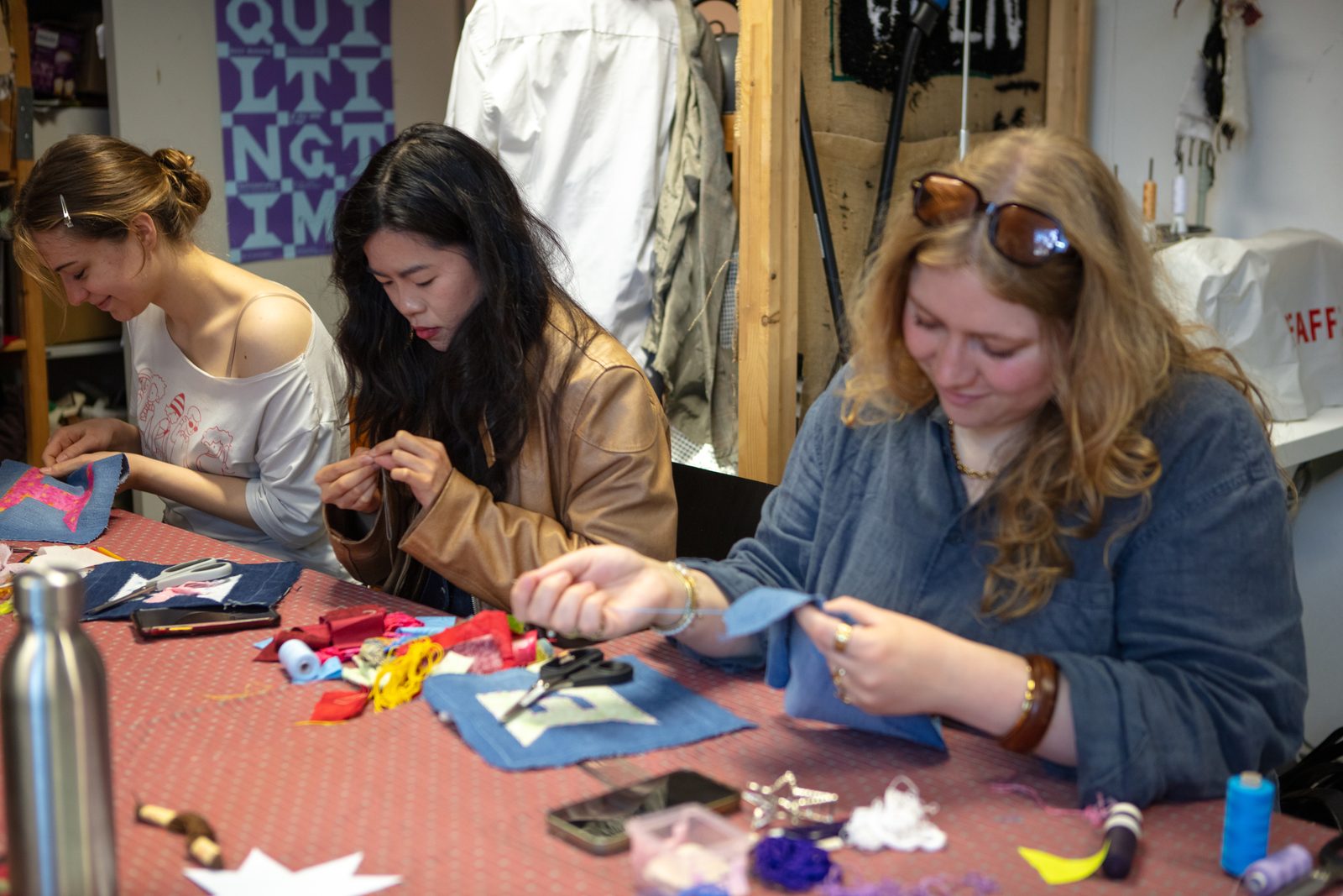 Three participants sewing hand-cut fabric letters together at an outdoor table.