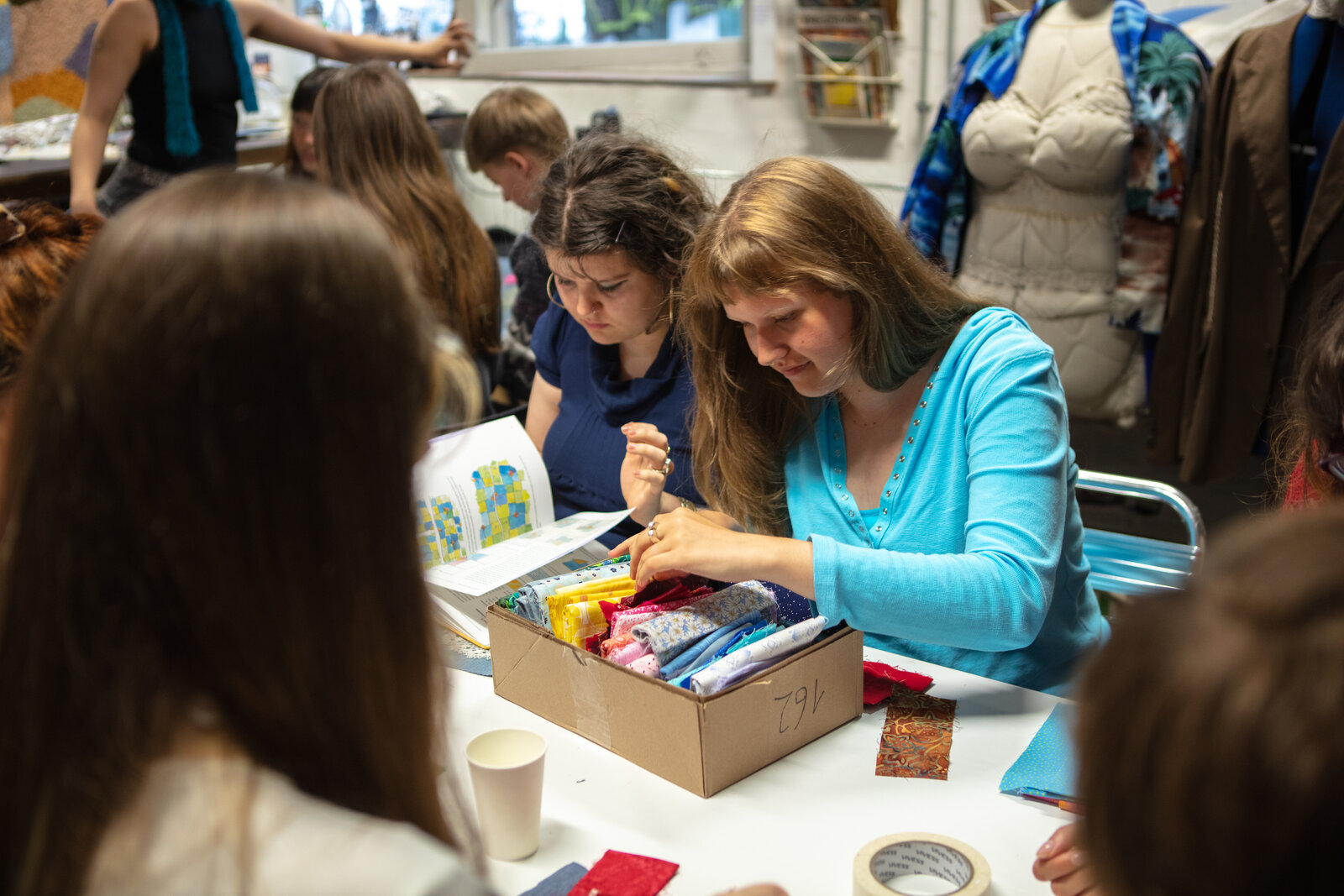 Two participants picking fabric scraps from a box while sewing letters together.