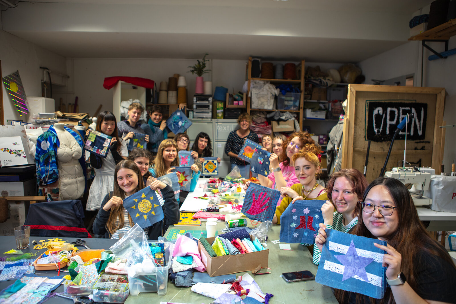 The whole workshop group indoors, each holding up their finished quilt square.
