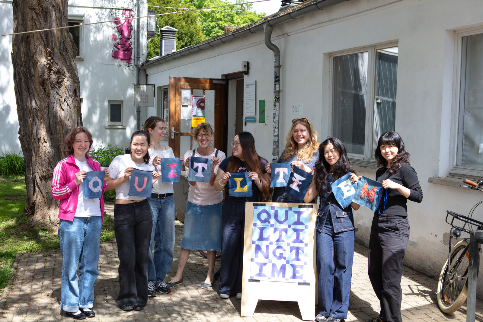 The workshop group standing outside, each holding a hand-sewn fabric letter that together spell QUILTING TIME.