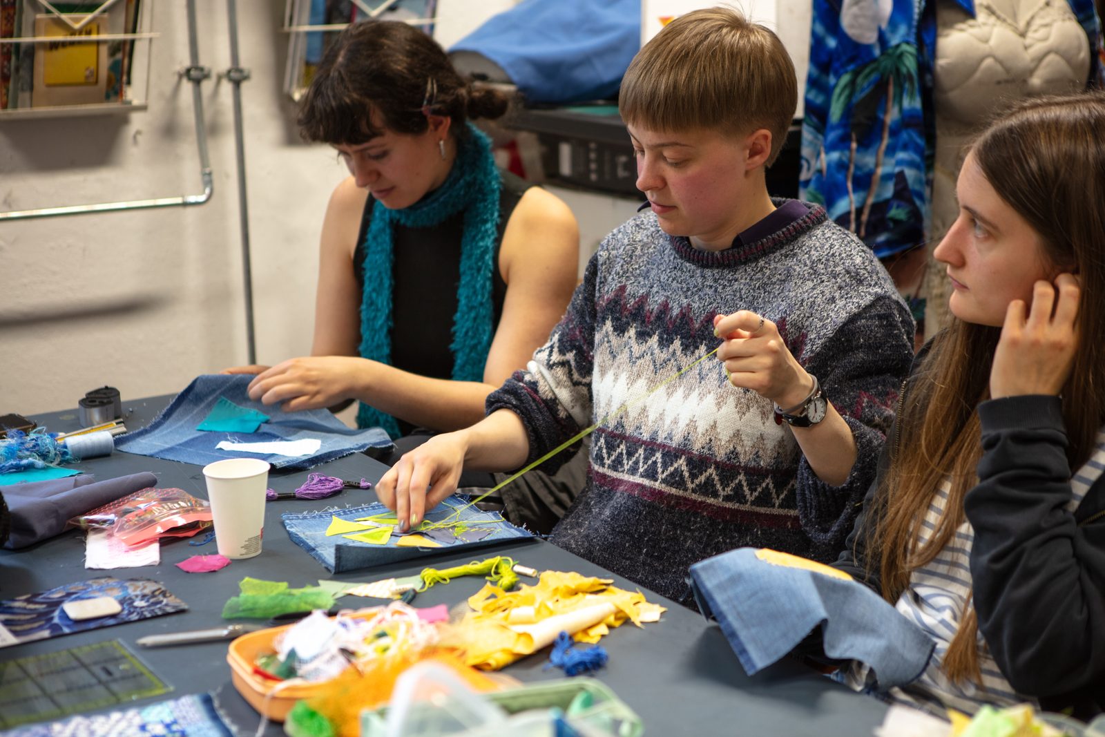 Three participants sitting together at a table, sewing fabric letters.