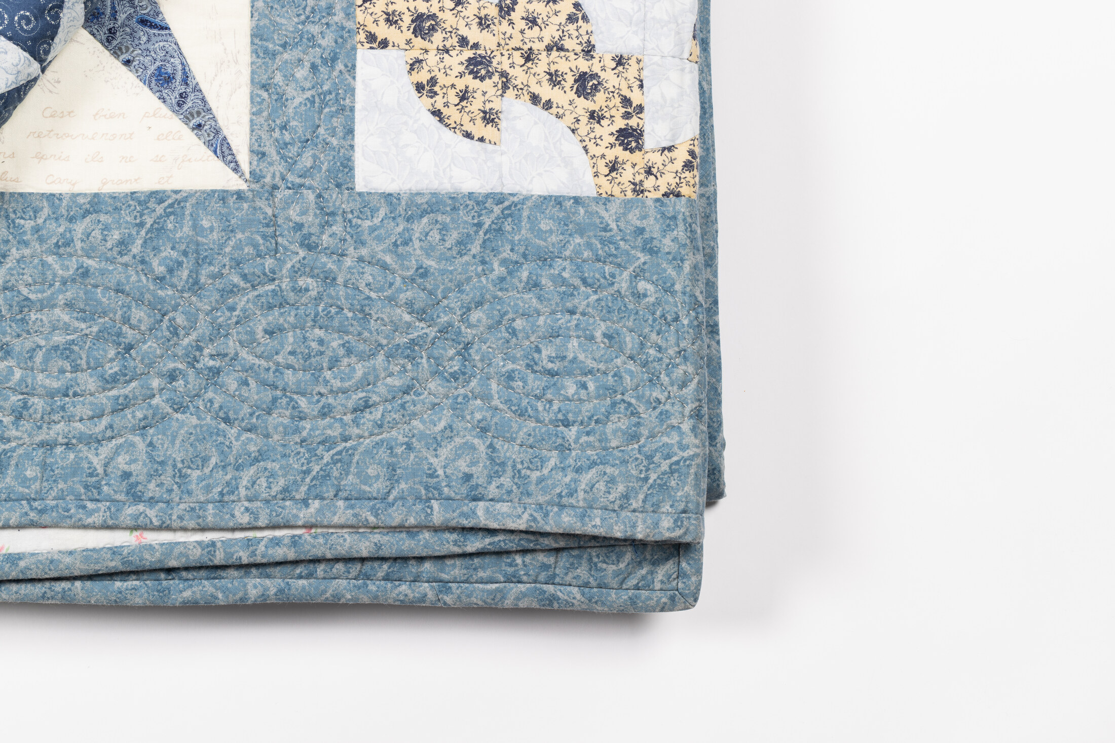 A folded corner of the quilt showing its paisley border fabric and a strip of cursive script fabric.