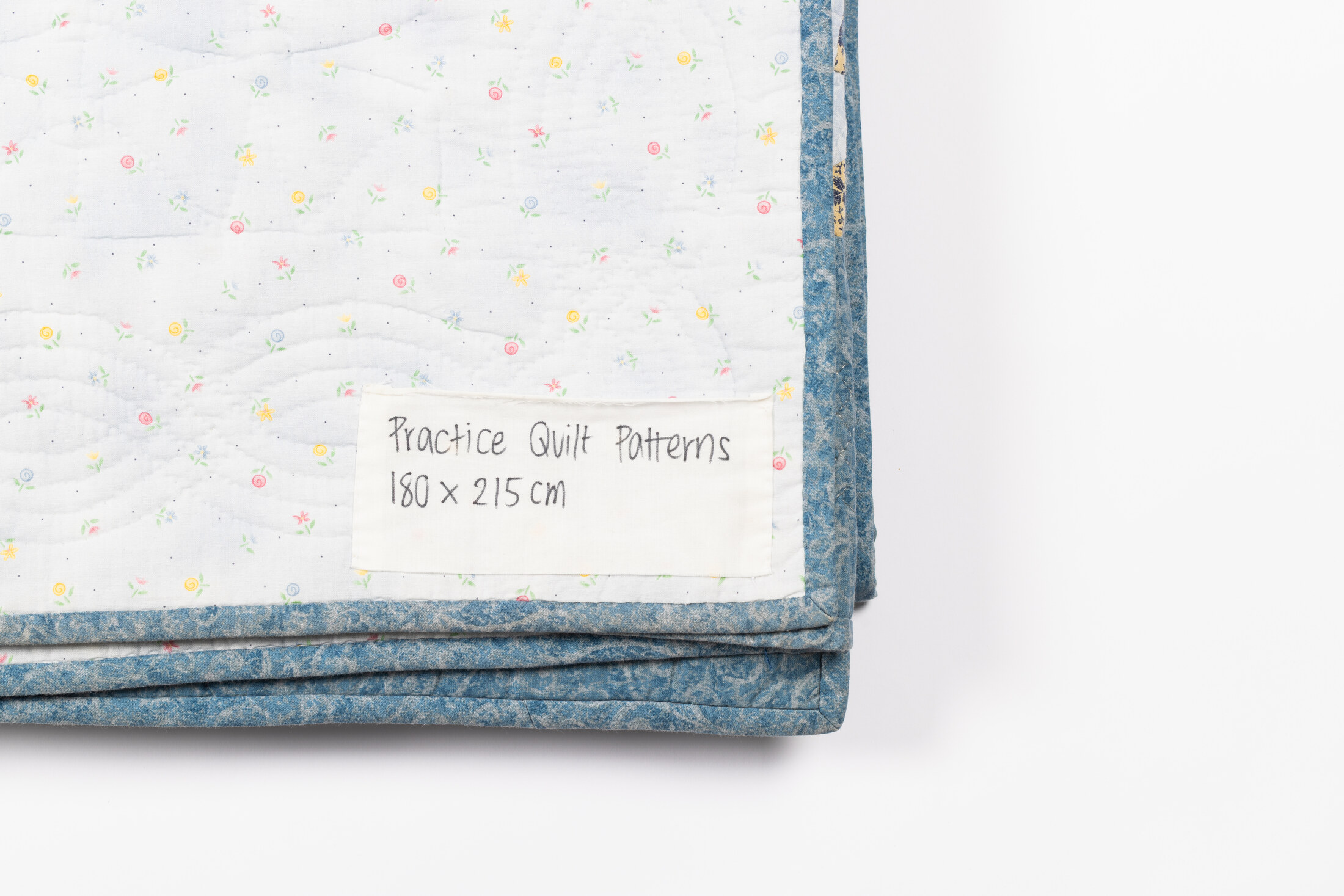 A hand-lettered fabric label reading Practice Quilt Patterns, 180 x 215 cm, stitched onto the quilt's floral backing.