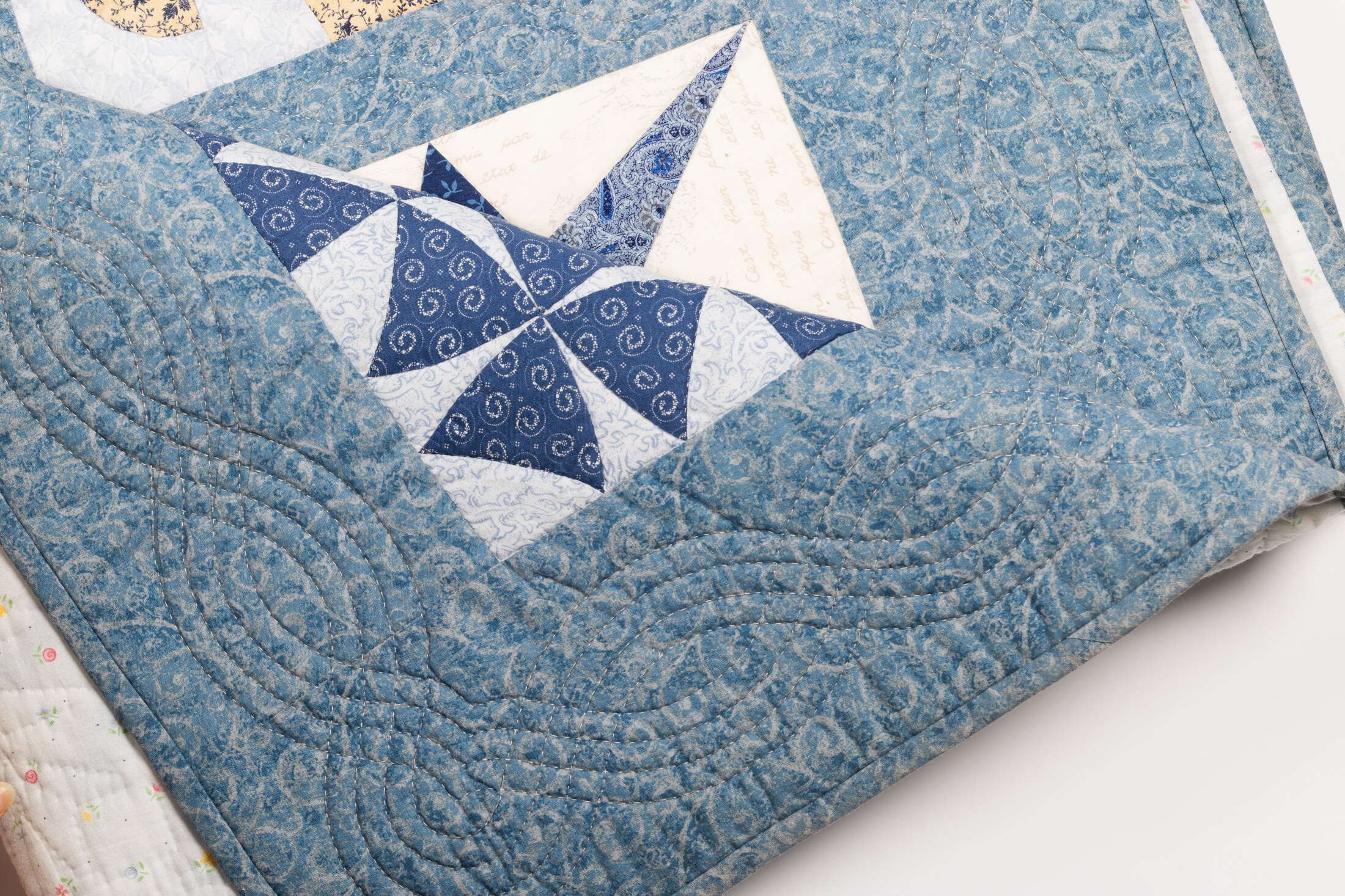 A macro view of a pinwheel block in navy and pale blue fabrics, with visible quilting stitches on the border.