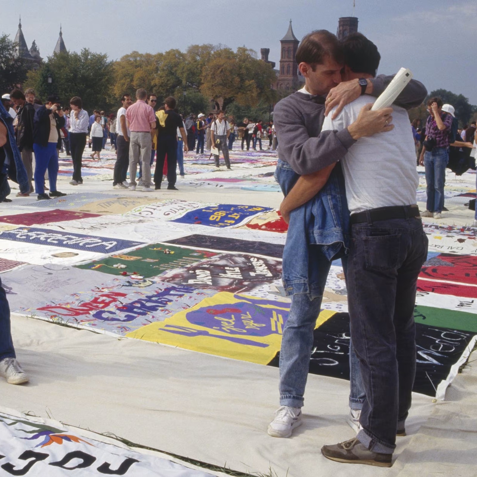 Two men embracing amid the panels of the AIDS Memorial Quilt laid out on the National Mall.