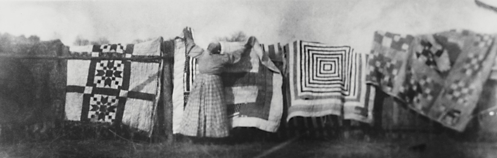 A black-and-white panoramic photograph of quilts hanging together on a clothesline.